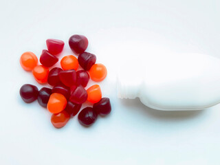 Group of red, orange and purple multivitamin gummies with the bottle isolated on white background....