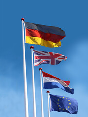 Naklejka premium Flags of Germany, United Kingdom, France and the European Union on flagpoles. Flag of Germany is on top. Blue sky background.