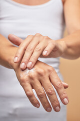 For dry skin. Vertical shot of a woman rubbing moisturizer on hands on beige background