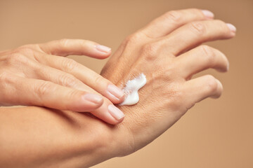 Obraz na płótnie Canvas Female hands with nude manicure on nails applying hand cream