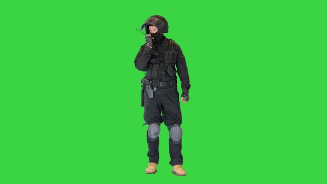 Special forces soldier in black uniform speaking on the radio on a Green Screen, Chroma Key.