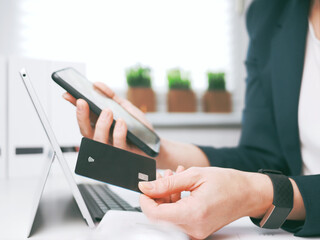 young woman holding credit card and using laptop and smartphone. Online shopping, booking and banking concept. Businesswoman or entrepreneur in the home office.