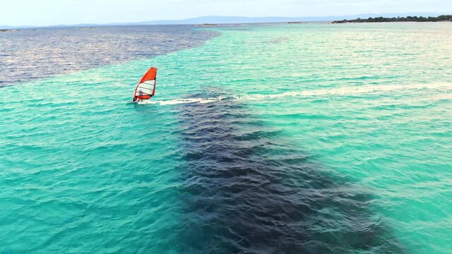 Aerial drone view of a man at windsurfing in Aegean sea. Transparent water, land with greenery in Greece