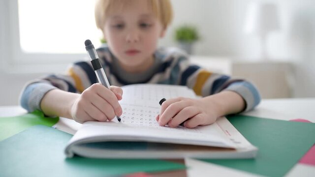 Elementary student boy doing math homework at home.Child learning to count, solves arithmetic examples, doing exercises in workbook. Preparing preschooler for school.Education for kids.Focus on hand