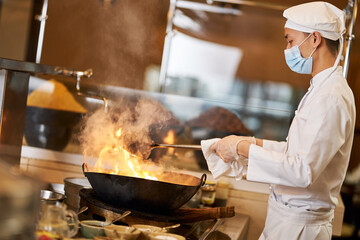 Professional Asian chef making stir-fry in flaming wok