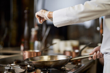 Chef in white uniform salting his cooking in the pan