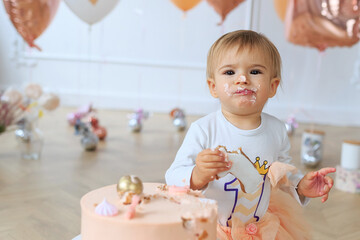 Close up Cute blond baby girl in peach tutu sitting next to on festive background by smashed...