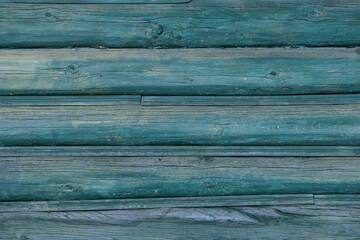 An old wall of pine logs. Weathered, faded wood. Green paint faded in the sun. Factura of a tree.