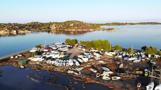 Aerial drone view of an island in Aegean sea with multiple beached yachts and boats, rocks, greenery around, sunset, Greece