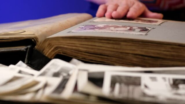 Elderly woman looks through an family album with old photos at table at home.