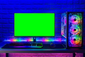 colorful bright illuminated rgb gaming pc with keyboard mouse monitor with green screen copy space front of LED light brick stone wall. Computer playing hardware games background