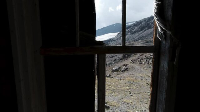 View through ruined window on mountainous landscape. Clip. Looking through old wooden window without glass on beautiful mountain slope and blue sky. 