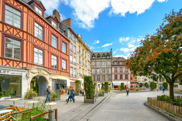Fototapeta na wymiar Timber frame homes line a town square in the medieval city of Rouen France with shops, a sidewalk cafe and tourists enjoying a sunny autumn day