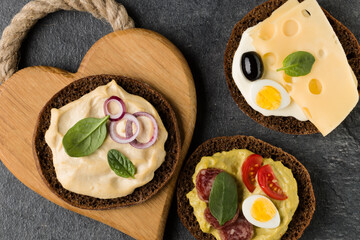 Open  faced  sandwich canape or crostini on a wooden serving board on dark stone background closeup. Top view.
