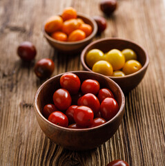 Cherry tomatoes of different colors in wooden bowls on a rustic table, close up view