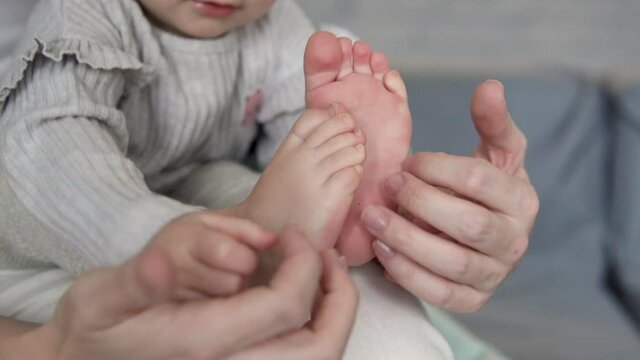 Little Baby Girl Touching Her Legs Playing With Toes, Sitting On Mothers Knees