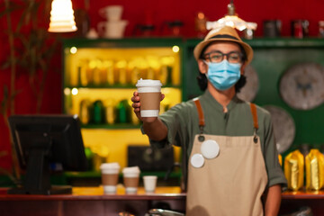 Barista with mask delivering coffee in a disposable cup.