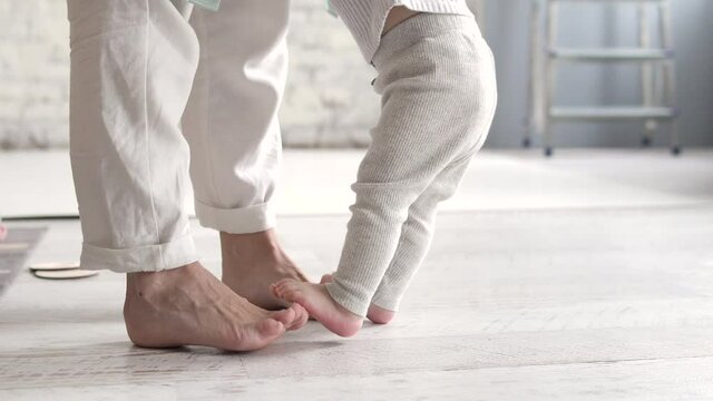 Little baby legs standing on adult ones, parent making steps with kid on legs