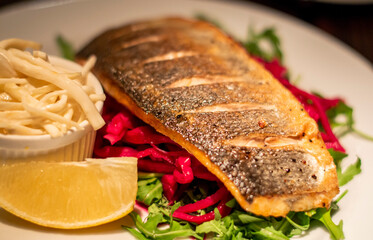 Delicious pan-fried fish fillet with vegetables and lemon on white plate.