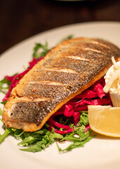 Delicious pan-fried fish fillet with vegetables and lemon on white plate.