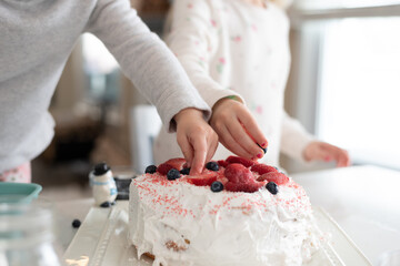 Closeup of two little girls decorating a cake with fruit - Powered by Adobe