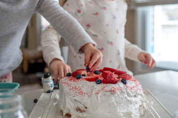 Two little girls decorating a cake with whipped cream and berries