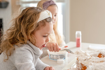 Two little girls frosting a cake with whipped cream