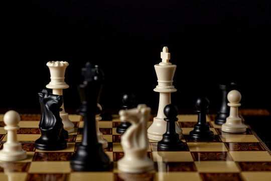 Image showing an ongoing chess game featuring a late game position. Versatile image for competition, ambition, struggle, defeat, victory, strategy concepts. A dark moody setting with wooden board.