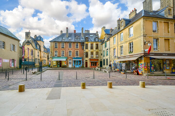 The small square outside the entrance to the Bayeux Cathedral, with colorful shops and cafes in the Normandy town of Bayeux, France. - obrazy, fototapety, plakaty