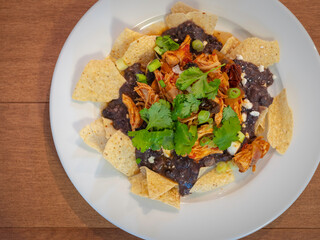 Homemade chicken meat, nachos, beans, and vegetables on a white plate