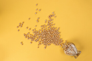 Soyabeans pouring from hart shape glass bottle on yellow background