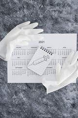 covid-19 vaccine against the pandemic, 2021 calendar with syringe sketch on notepad and disposable gloves on it