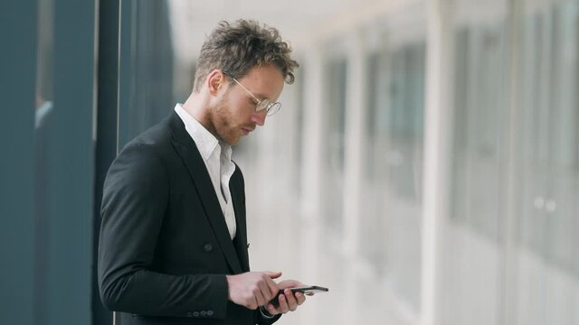 curly man in glasses with a phone in a glass corridor