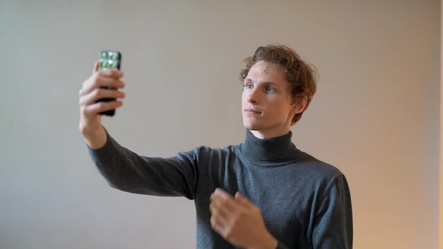 Handsome young curly guy examines a hairstyle on a smartphone