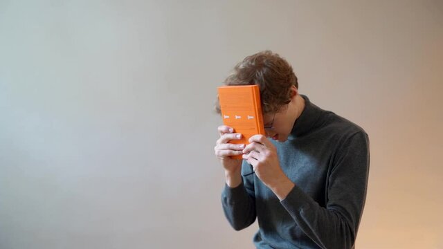A young curly guy hits himself on the head with a book