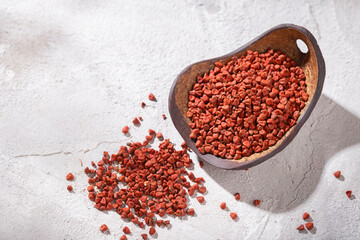 achiote grains in wooden bowl on white background (Bixa orellana)