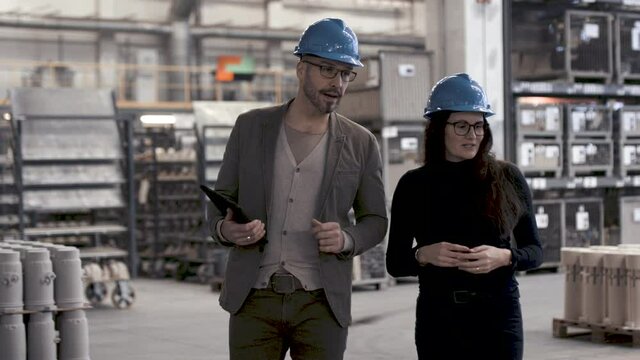Mann f&uuml;hrt Frau durch eine Industriehalle
