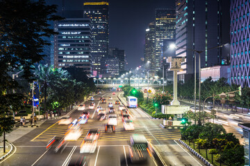 Fototapeta premium Traffic, captured with blurred motion, rushes along the Thamrin avenue in the heart of Jakarta downtown district in Indonesia capital city at night.