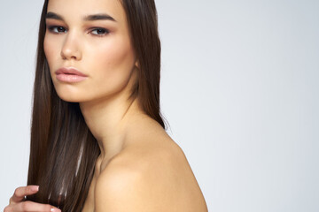 Pretty brunette naked shoulders long hair close-up light background