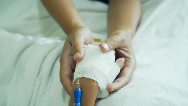 Young mother is holding hand bandaged of little daughter with comforting while they lying in the hospital bed sleeping. Recovering little girl. Hopeful emotional moment in ward. Focus on the hands.
