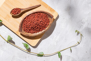 achiote grains in wooden bowl on white background (Bixa orellana)