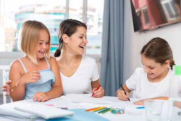 Fototapeta premium Woman with two kids drawing together sitting at table in living room