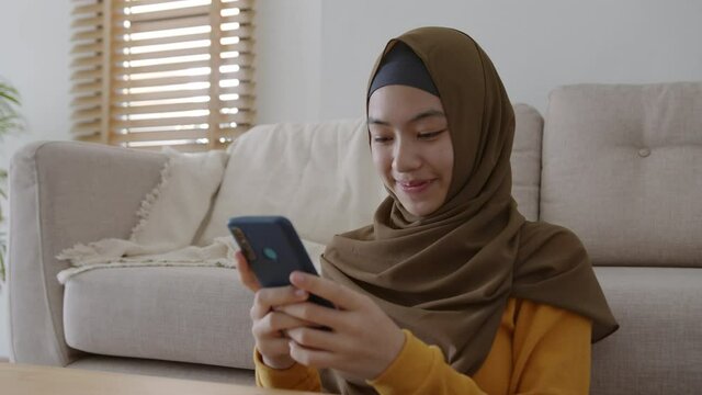 Happy Muslim girl wear hijab using texting smartphone or chat at home 