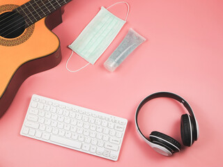 flat lay of acoustic guitar, white headphones computer keyboard, protective mask and sanitizer gel...