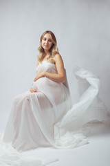 Fototapeta na wymiar Elegant pregnant young woman standing wearing flying white fabric. Pregnancy, maternity and motherhood concept.
