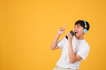 Happy young man singing while using earphones and mobile phone isolated over yellow background.