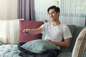 Young Asian man enjoying his holiday watching TV at home.