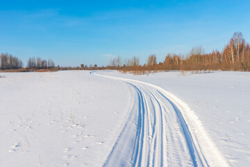 Snowmobile road on a snowy field. Winter landscape on a bright sunny day