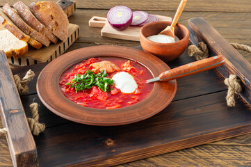 Borsch - traditional Ukrainian and Russian beetroot soup on dark wooden background. Served with rye bread, garlic and salt on wooden tray