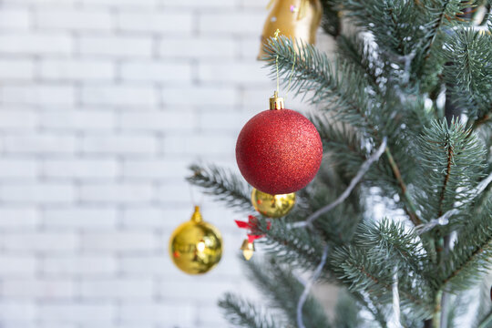 Closeup of beautiful little Chrsitmas baubles as red and golden glass ball is hanging on Christmas tree branches in front of grey wall in living room in holidays as Chrsitmas eve or new years.